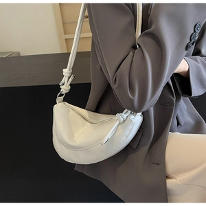 Close-up of a white crescent crossbody bag featuring handcrafted side knot details on a model
