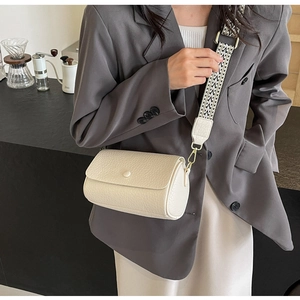 Detail of off-white cylinder crossbody bag with a patterned wide fabric strap and gold hardware