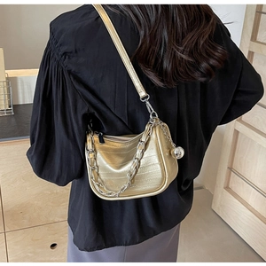Détail du sac doré aspect crocodile avec chaîne argentée et pendentif boule en métal