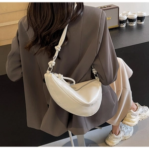 Close-up of a white hobo bag with knotted strap detail against a minimalist urban background