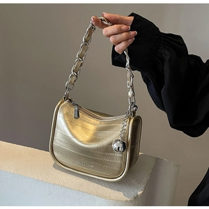 Détail du sac sous le bras doré clair texturé avec chaîne argentée et breloque en métal