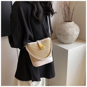 Detailed view of woven straw bucket bag with white leather trim and gold metal clasp