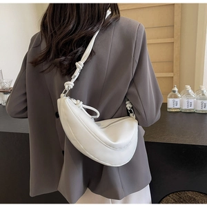 Detail of a white half-moon shoulder bag with a unique knot detail on the strap