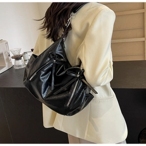 Detail of black glossy leather bucket bag with ribbon bow zipper pull and silver hardware