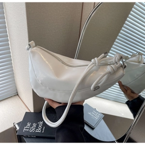 Detail of white crescent bag with knotted shoulder strap and glossy finish in soft light
