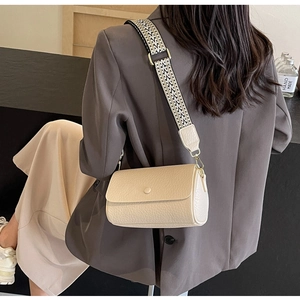 Detail of cream crossbody bag featuring a wide geometric woven strap and gold metal buckles