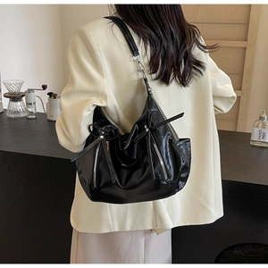 Detail of black glossy bucket bag featuring silver zippers and decorative bow ties
