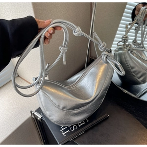 Close-up of a silver crescent handbag with glossy metallic finish and knotted strap