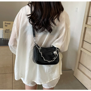 Détail d'un sac en cuir noir texturé avec chaîne argentée et charm boule sur un mannequin