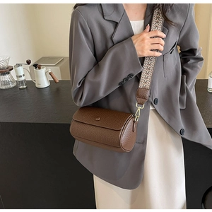 Detail of cylindrical brown pebble leather crossbody bag with geometric woven wide strap