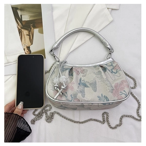 Detail of floral embroidery and metallic top handle on a white hobo bag with pearl beads