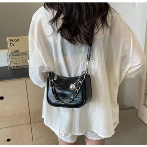 Détail d'un sac bandoulière en cuir noir texturé avec chaîne argentée et pendentif rond