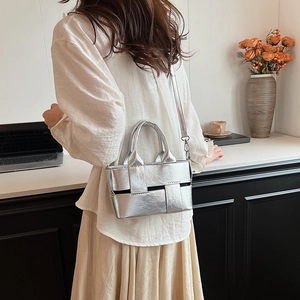 Silver woven handbag with detachable strap shown in a modern home office setting