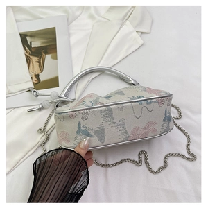Detail of embroidered crane handbag with metal handle and chain strap on white fabric