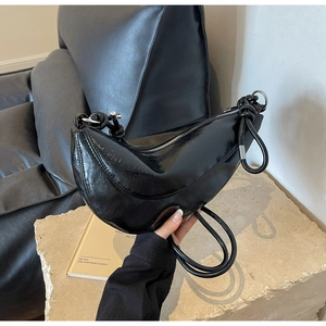 Detail of black crescent shoulder bag featuring glossy patent leather and knot strap
