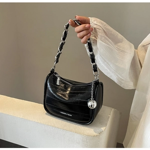 Détail d'un sac à bandoulière en cuir verni noir avec chaîne argentée et boule métallique