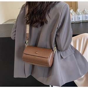 Brown cylinder crossbody bag with wide ethnic woven strap and lychee grain leather