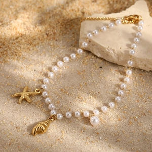 Detailed shot of starfish and shell pendants on a pearl anklet over beach sand