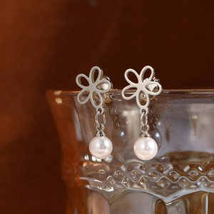 Orecchini a fiore d'argento con perle appesi a un bicchiere di vetro ambrato vintage