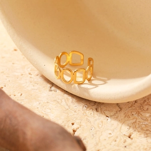 Detail shot of golden open ring with geometric cut-outs on stone texture background