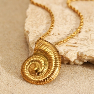 Golden spiral conch pendant necklace on natural sand and rock background