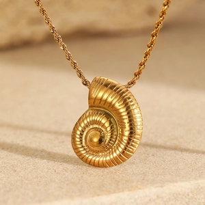Macro shot of gold spiral conch pendant on sand showing polished metal texture