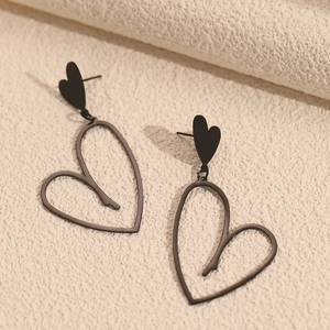 Gros plan de boucles d'oreilles pendantes cœur noir sur un fond beige texturé