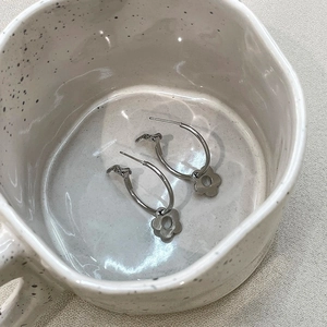 Detailansicht der silbernen Edelstahl-Creolen mit hohlen Blumenanhängern in einer Keramiktasse
