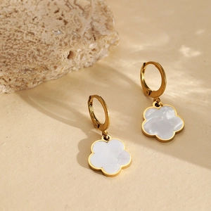 Golden hoop earrings with natural shell flower charms on a warm textured stone background