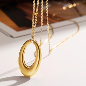 Macro view of gold hollow oval pendant with satin matte finish and fine cross chain