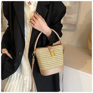 Detail of woven straw bucket bag with beige leather trim and gold metal twist lock closure