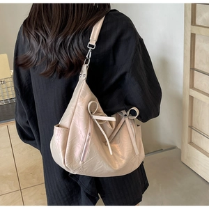 Detail of beige hobo bag with pleated pearlescent fabric and ribbon bow accent