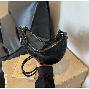 Detail of glossy black crescent bag featuring a unique knotted handle and silver zipper