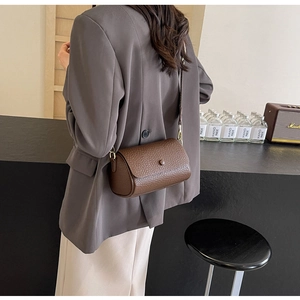 Close-up of brown cylindrical crossbody bag with pebbled leather and wide strap