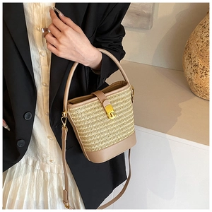 Detail of hand-woven straw bucket bag with beige leather strap and gold buckle