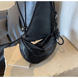 Detail of black glossy crescent bag featuring unique knotted straps and metallic accents