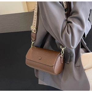 Detail of a brown cylindrical crossbody bag with lychee texture and geometric wide strap