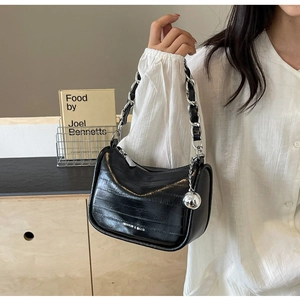 Détail d'un sac baguette en cuir noir brillant avec chaîne argentée et breloque boule