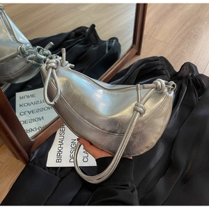 Detail of silver metallic crescent bag featuring pleated texture and knotted shoulder strap