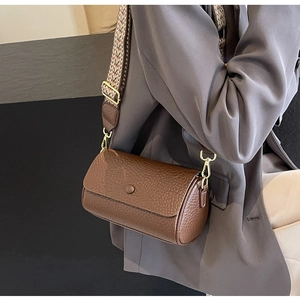 Detail of a brown cylindrical crossbody bag with a patterned wide strap on a model