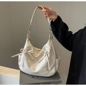Detail of white glossy bucket bag with bows and silver zippers on a business book