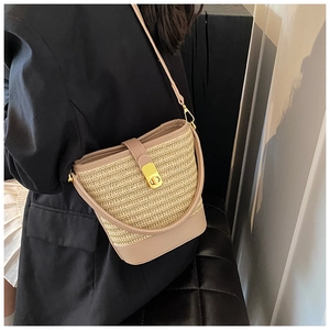 Close-up of woven straw bucket bag with beige leather trim and golden metal lock