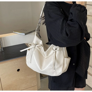 Detail of cream white hobo bag featuring decorative bows and a vertical zipper pocket