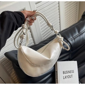 Detail of white glossy leather crescent bag featuring a knotted strap and silver hardware