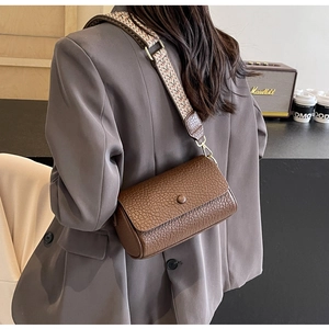 Detailed view of brown litchi pattern cylinder bag with retro geometric woven strap