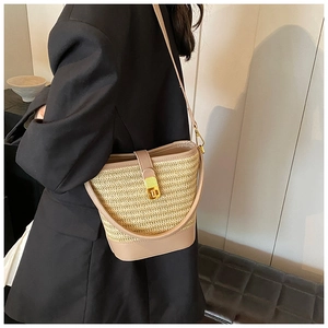 Model wearing straw bucket bag with khaki leather base and thin shoulder strap