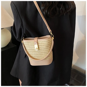 Detail of woven straw bucket bag featuring a brown leather strap and golden metal clasp