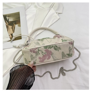 Detailed macro of vintage floral embroidery fabric on a mini white handbag with chain
