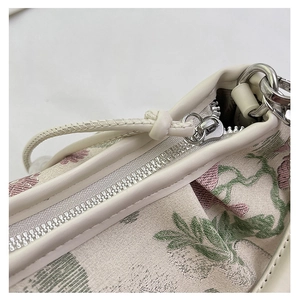 Detail of floral embroidery on beige fabric bag with silver metal zipper hardware