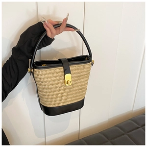 Close-up of woven straw bucket bag with black leather trim and golden metal clasp